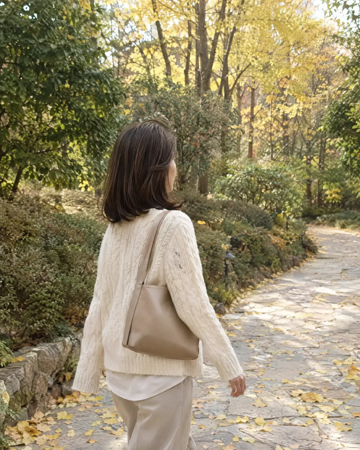은행잎이 떨어진 산책길을 걷는 어깨 길이 머리 여성의 옆뒷모습